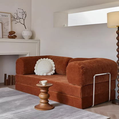 A brown soft velvet made teddy compression sofa that converts into a cozy bed in different forms. It is minimal with its straight shape yet soft edges giving a morocon, mid-century retro vibe to it. There are contrasts of steel frames on the side that gives off a bauhaus feel along with its lighter pastel shade of brown