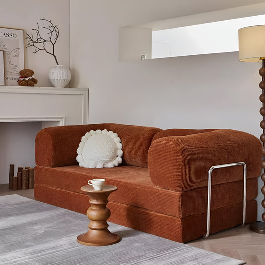 A brown soft velvet made teddy compression sofa that converts into a cozy bed in different forms. It is minimal with its straight shape yet soft edges giving a morocon, mid-century retro vibe to it. There are contrasts of steel frames on the side that gives off a bauhaus feel along with its lighter pastel shade of brown